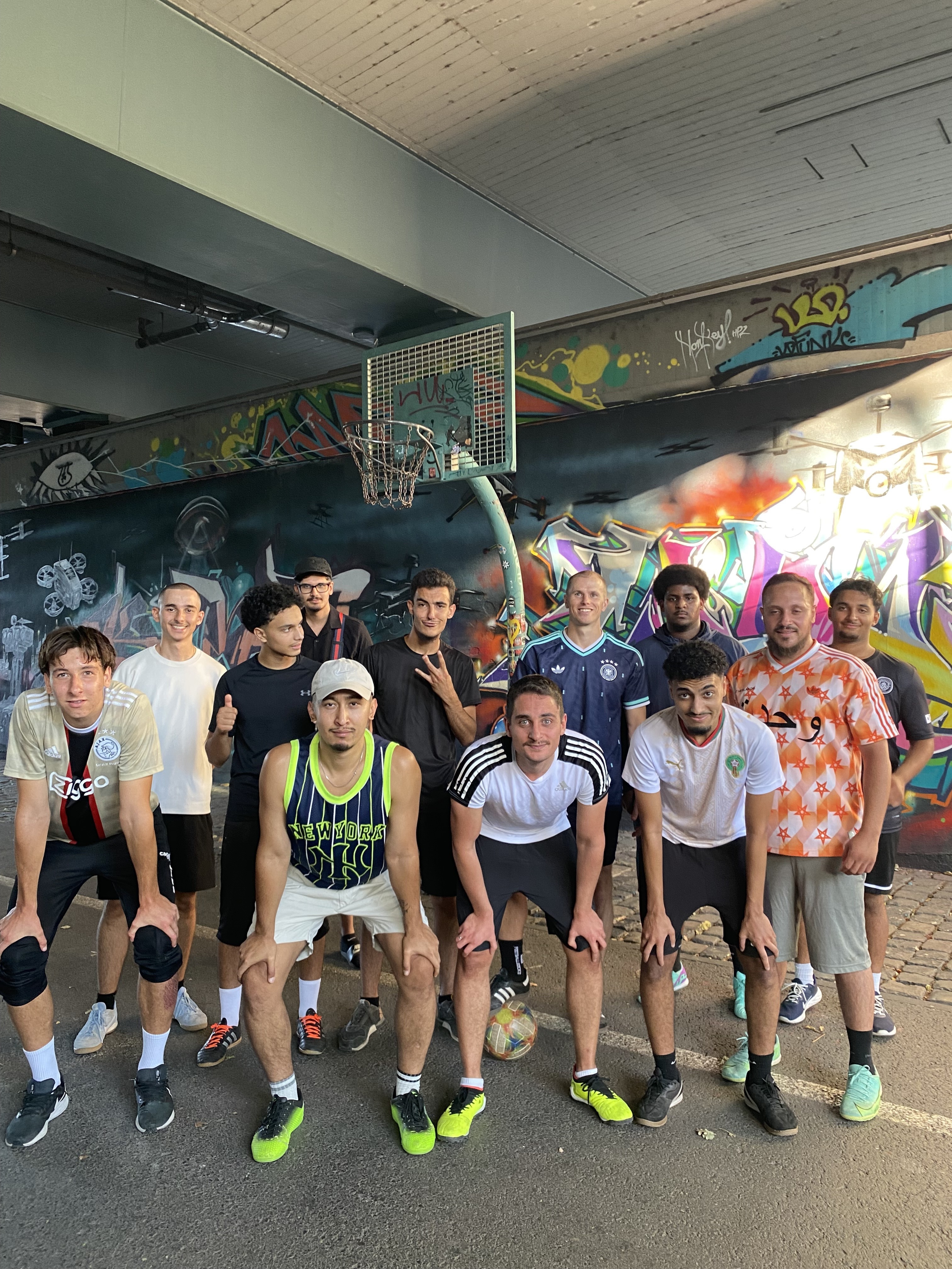 Gemischte Kickrunde beim Streetfußball unter einer Brücke